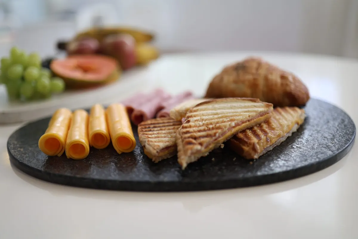 Café da manhã servido sobre pedra: queijo em rolinhos, misto-quente, croissant e frutas