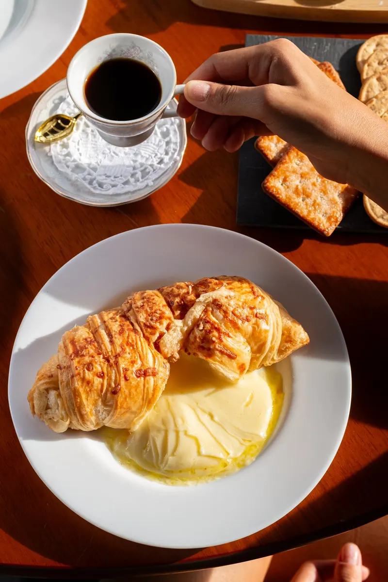 Croissant com manteiga derretendo e xícara de café