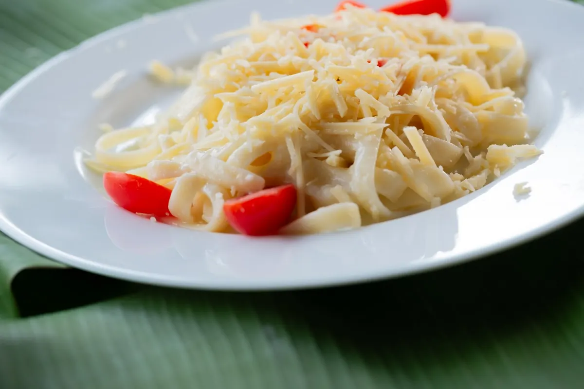 Prato de macarrão com queijo ralado e tomate-cereja sobre folha de bananeira