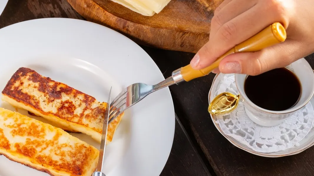 Queijo coalho grelhado no prato, com garfo e faca, ao lado de uma tábua de queijos fatiados