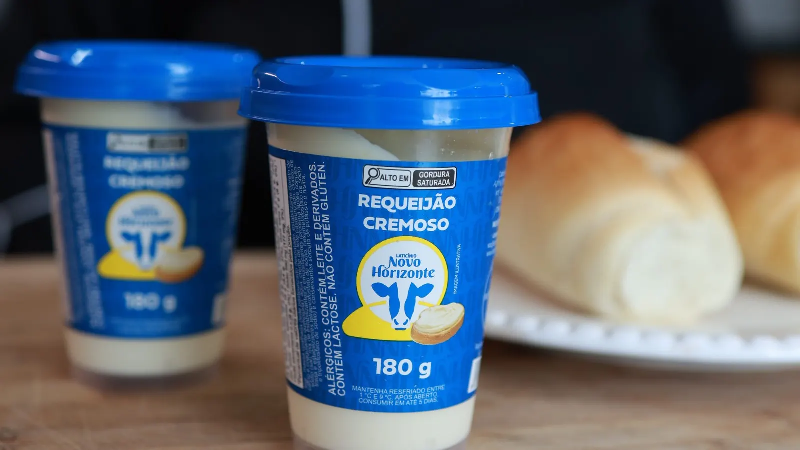 Dois copos de Requeijão Cremoso Novo Horizonte de 180 g ao lado de pães